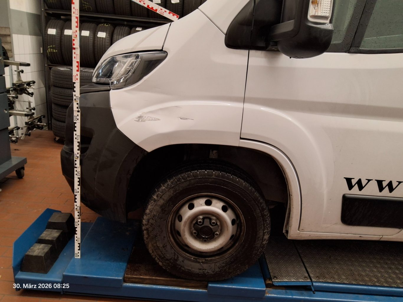 Fahrzeugprofil eines weißen Transporters auf einer Hebebühne mit einem Rad sichtbar.