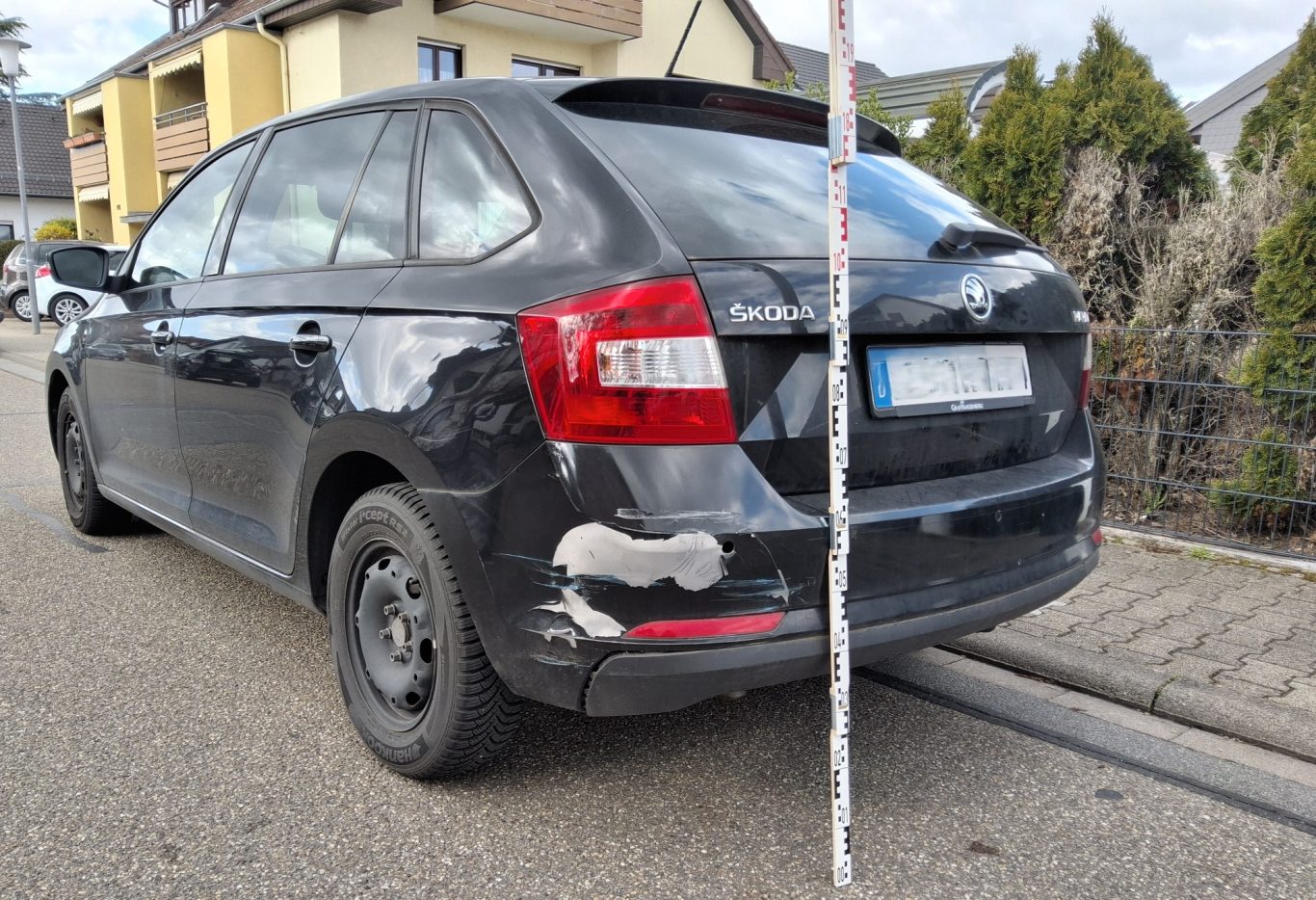 Schwarzes Auto mit Beschädigungen an der hinteren rechten Seite, geparkt auf der Straße.