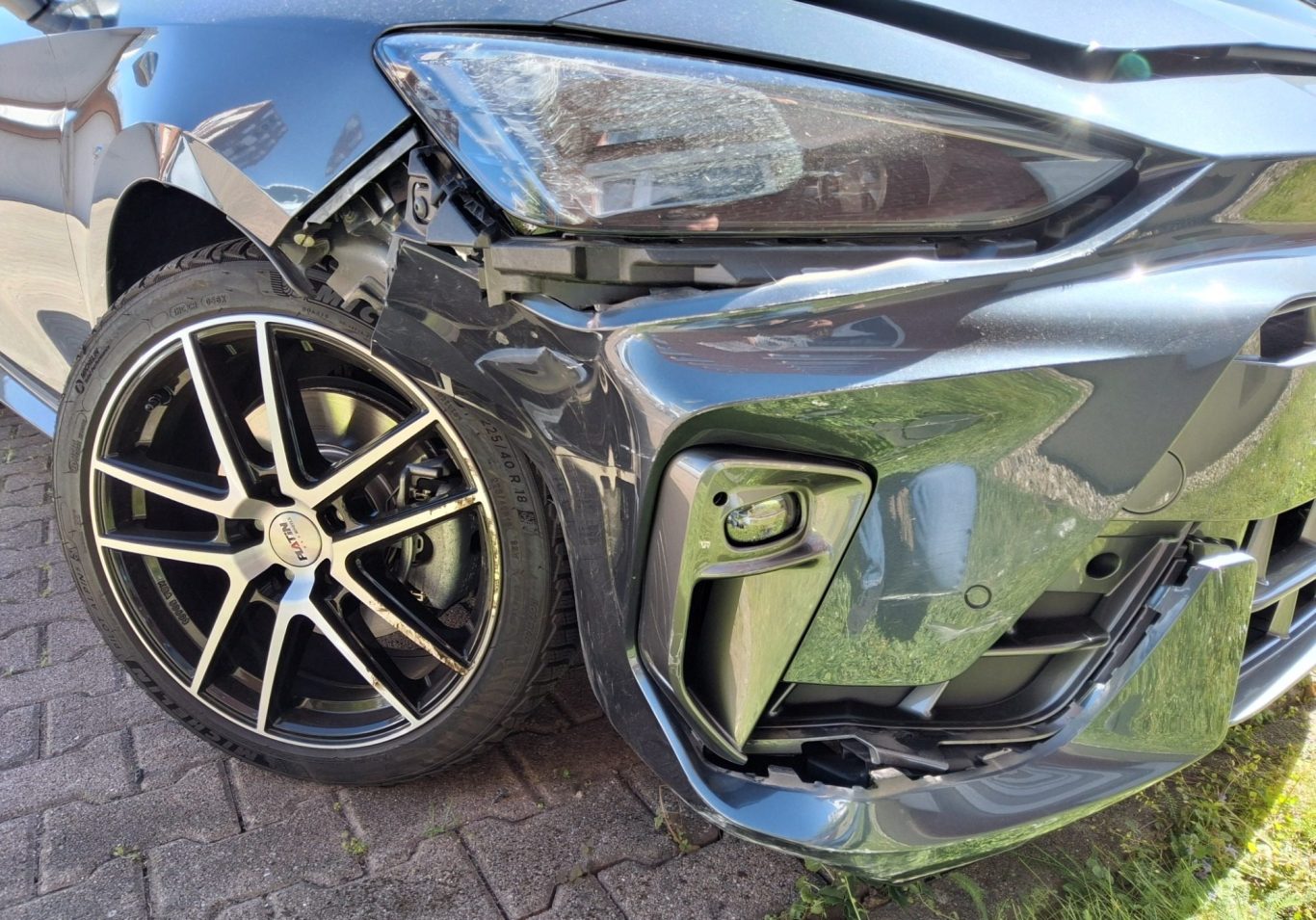 Vorderseite eines beschädigten Autos mit einem verformten Kotflügel und einer zerkratzten Felge.