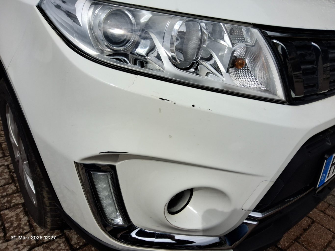 Kratzer an der vorderen linken Stoßstange eines weißen Fahrzeugs.